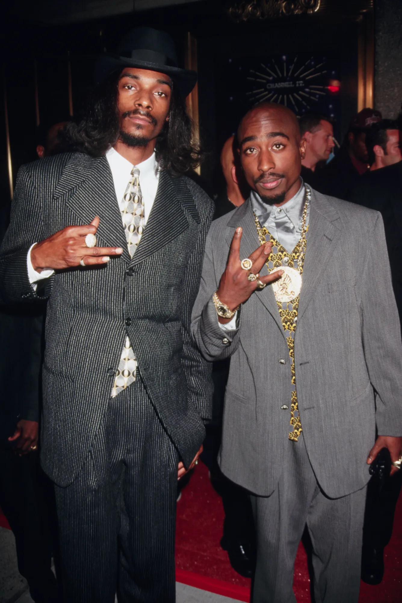 Tupac Shakur and Snoop Dogg wearing suits with gold chains, showcasing 1990s hip hop fashion and luxury streetwear style