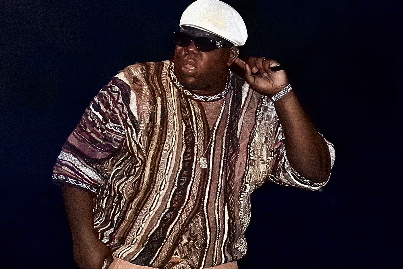 Image of The Notorious B.I.G. wearing a colorful Coogi sweater and sunglasses, showcasing his classic 90s luxury style.