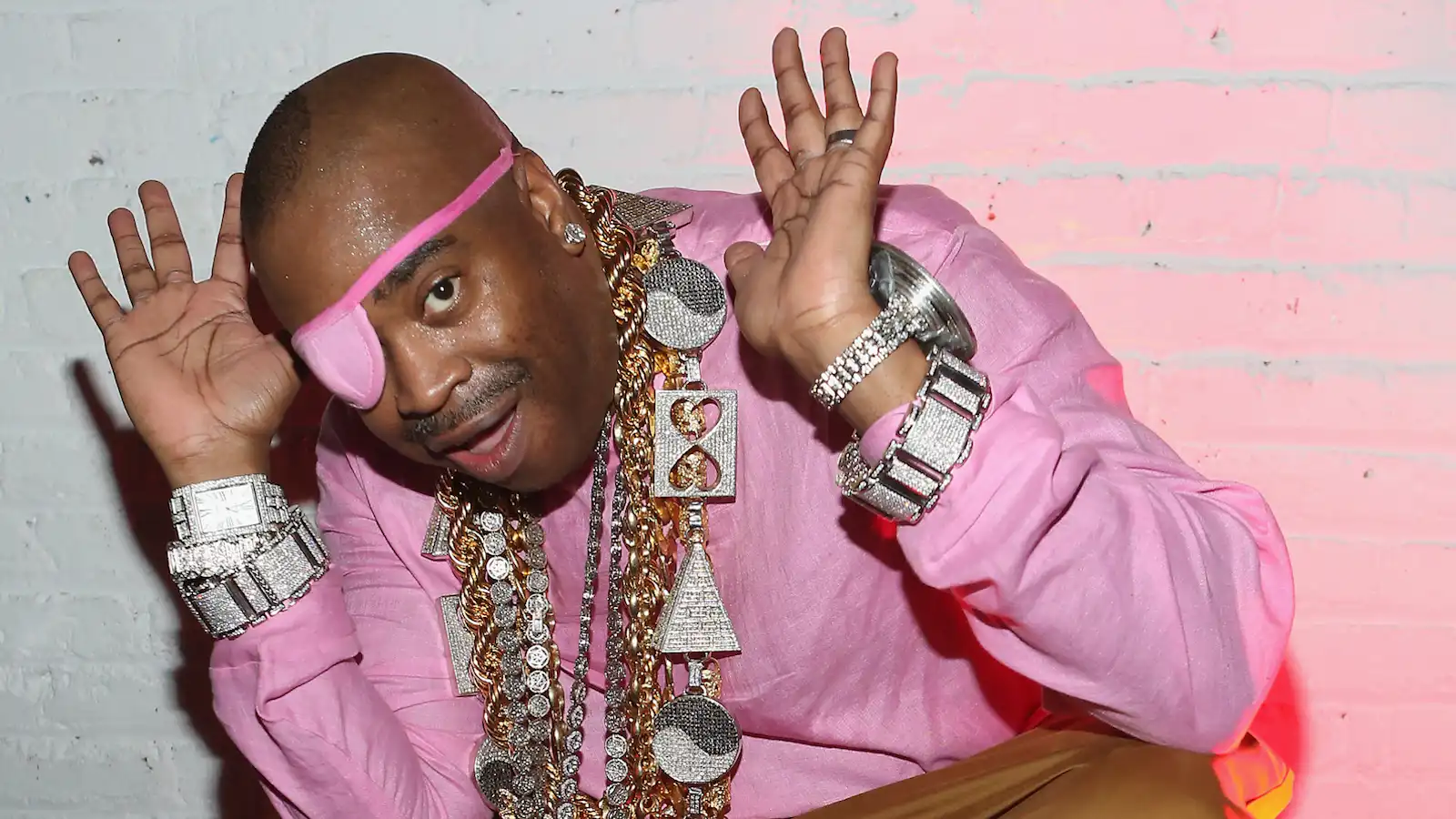 Photo of Slick Rick wearing oversized gold chains, pink shirt, and his signature eyepatch.