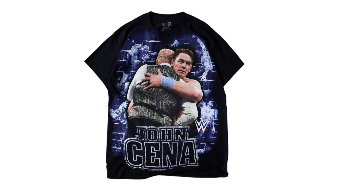Black graphic T-shirt featuring John Cena embracing an opponent in a WWE ring, part of the Complex x WWE John Cena streetwear collaboration.