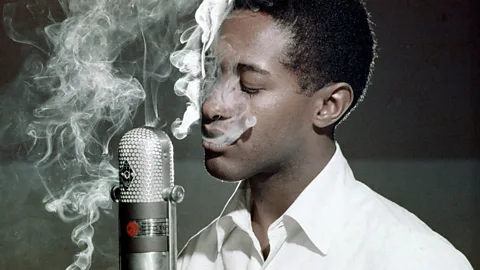 Sam Cooke singing into a microphone surrounded by smoke