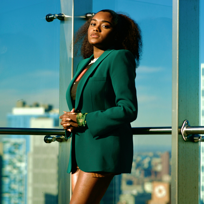 Tiffany James, founder of ModernBlkGirl, posing in a green blazer with a city skyline backdrop.