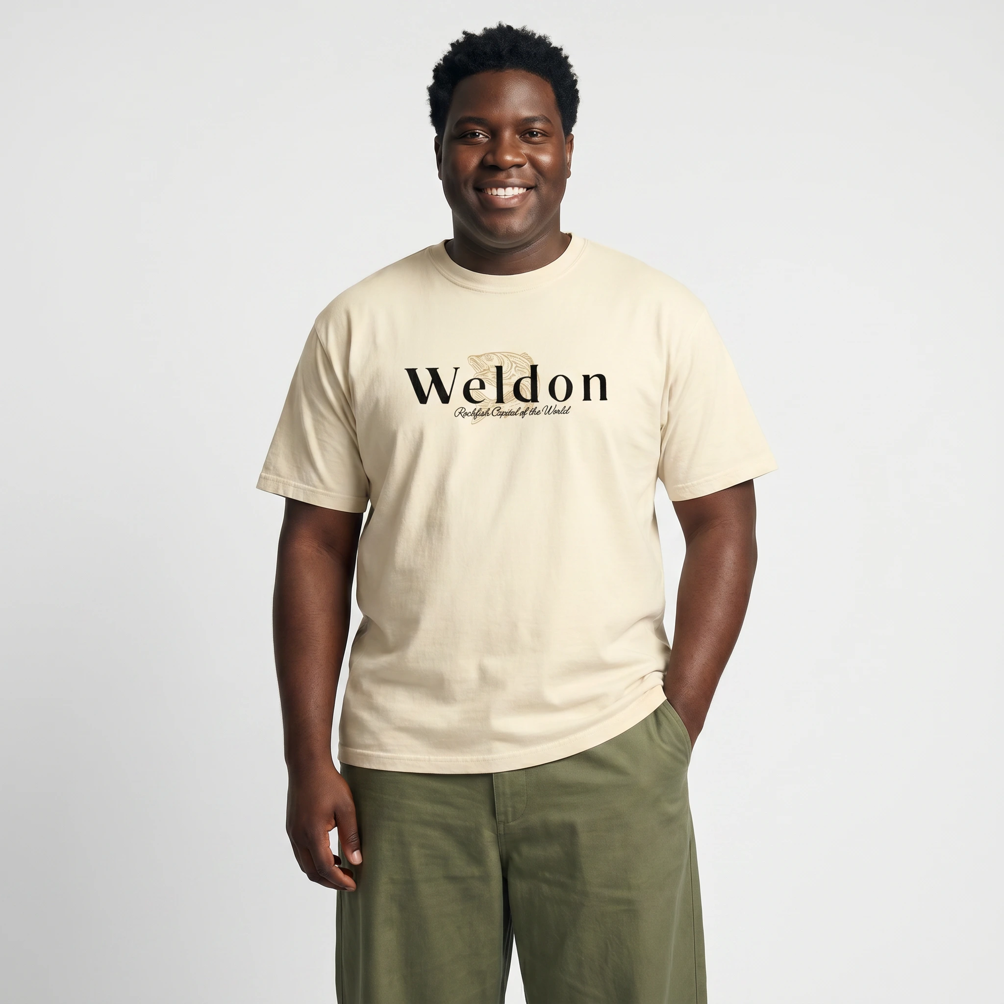Male model wearing the Mastuhree Brand Weldon Rockfish Capital of the World graphic t-shirt in ivory with olive green pants, celebrating Weldon, North Carolina heritage, fishing culture, and hometown pride through premium streetwear fashion.